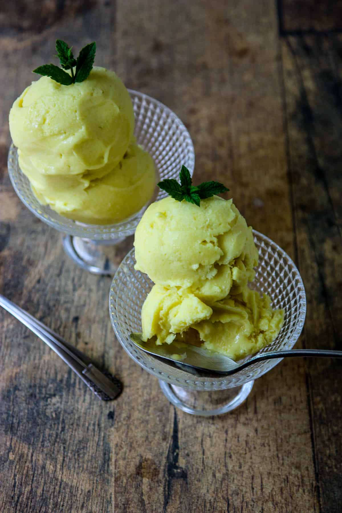 Two dishes of mango coconut ice cream on a wooden table top.