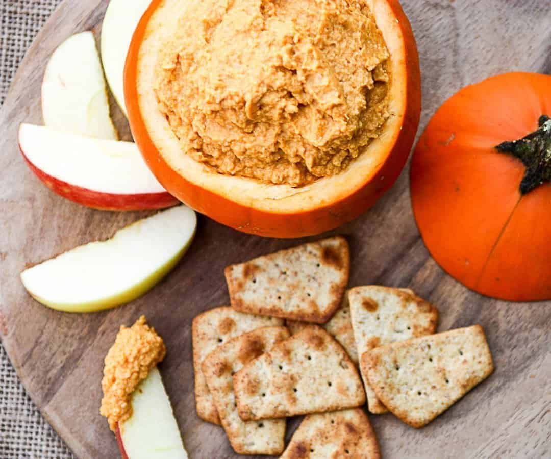 A hollowed-out pumpkin filled with dip, with apple slices and crackers