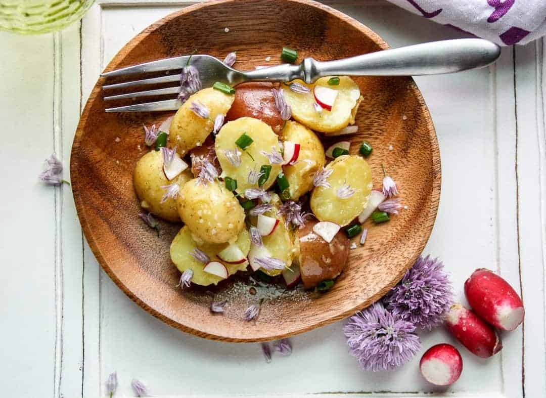 New Potato Salad with Chive Blossoms and Spring Radish on a wooden plate
