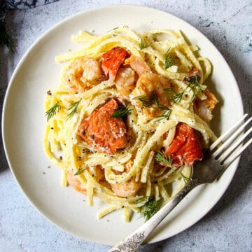 Shrimp and salmon alfredo on a white plate, with a silver fork.