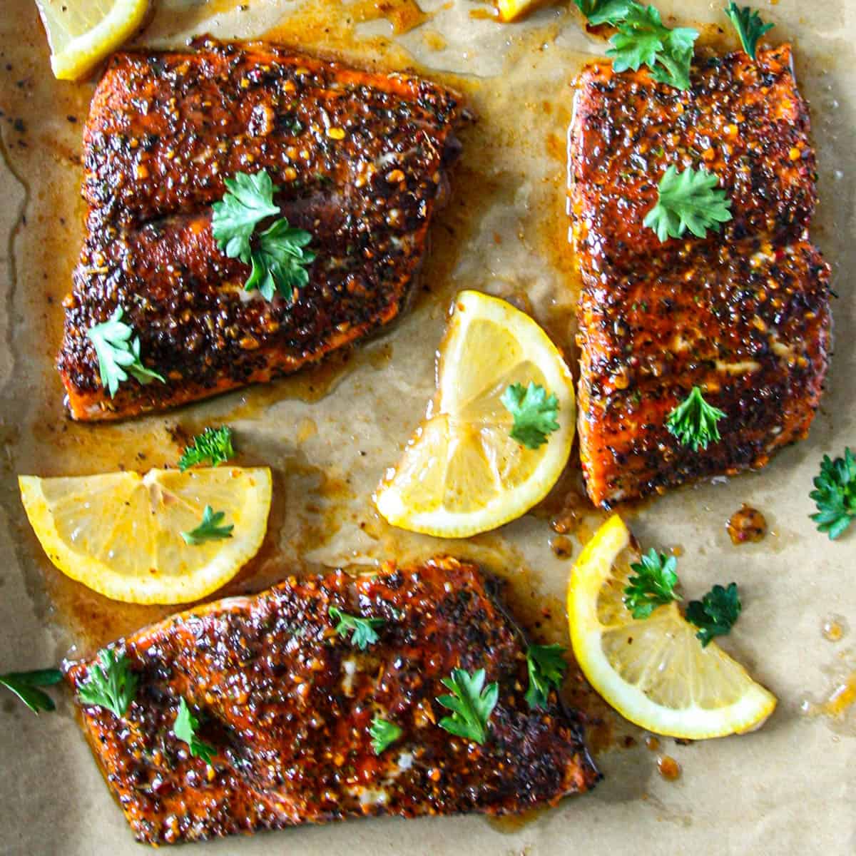 Three Cajun honey butter salmon fillets with lemon wedges.