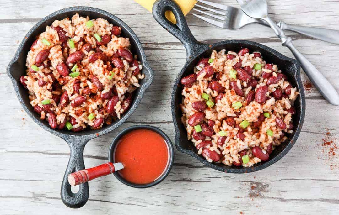 Two small black skillets filled with red beans and rice on wooden table