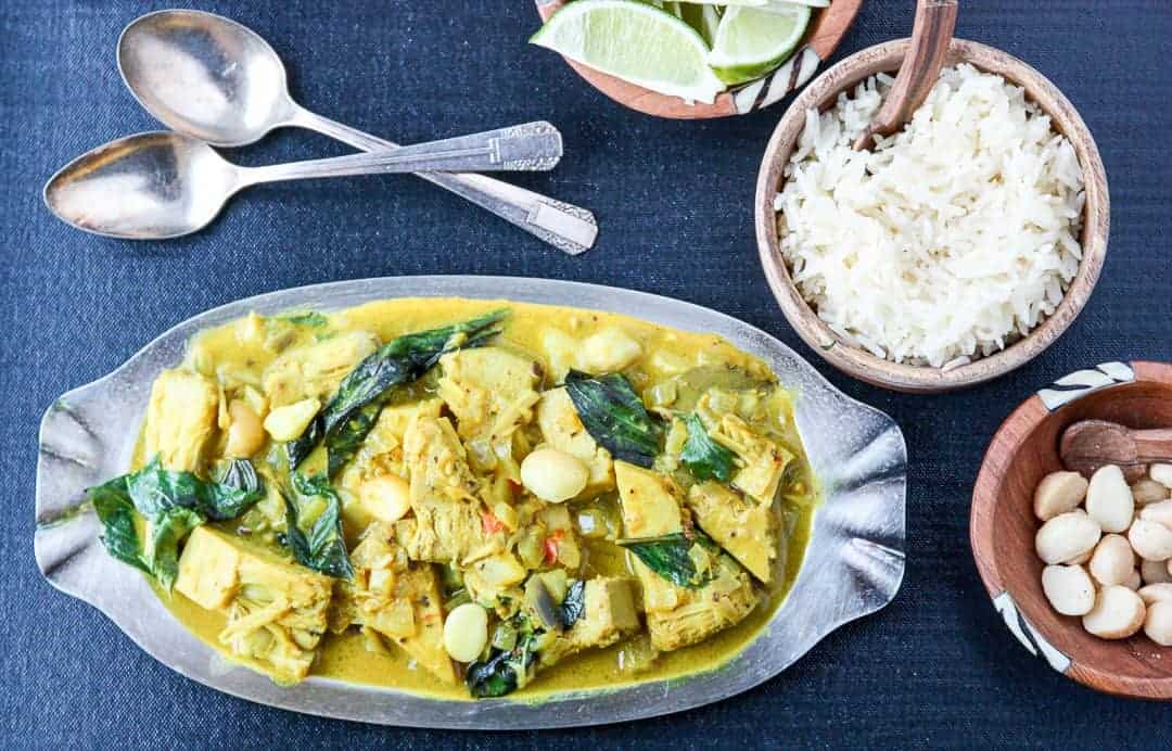 A plate of vegetarian curry on a table, with dishes of rice and lime wedges