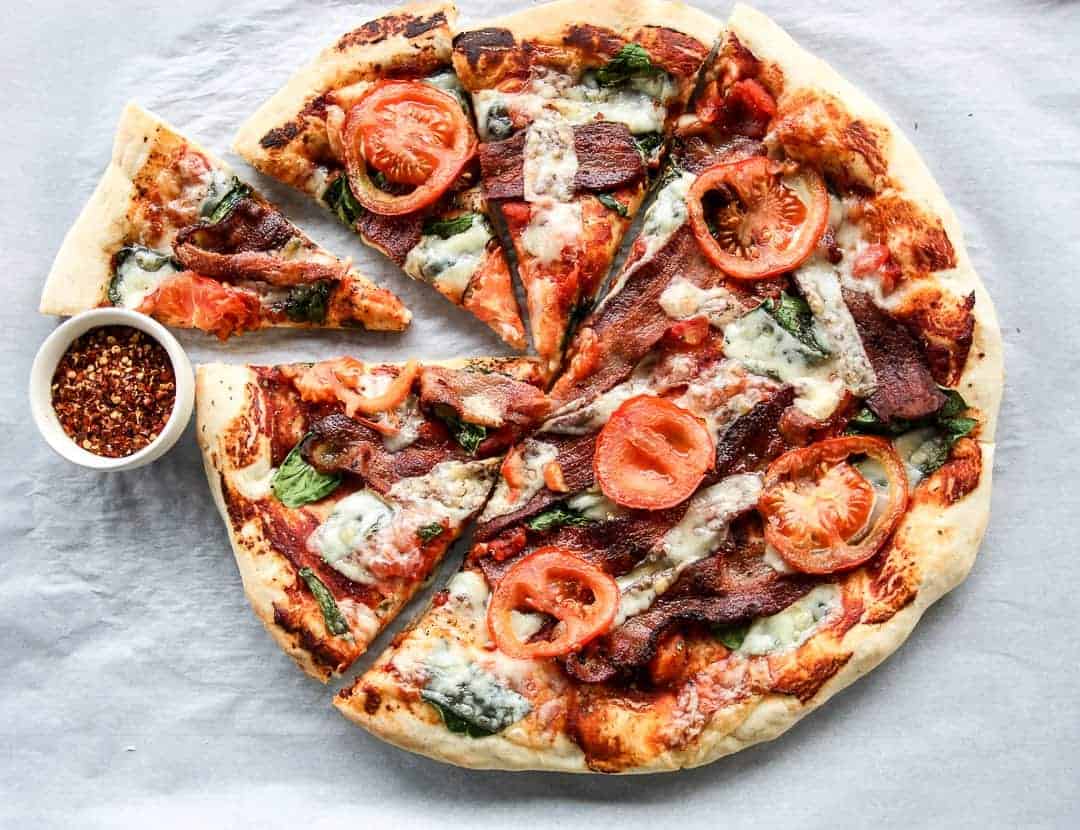 A pizza sitting on top of a cutting board, with Bacon and Tomato
