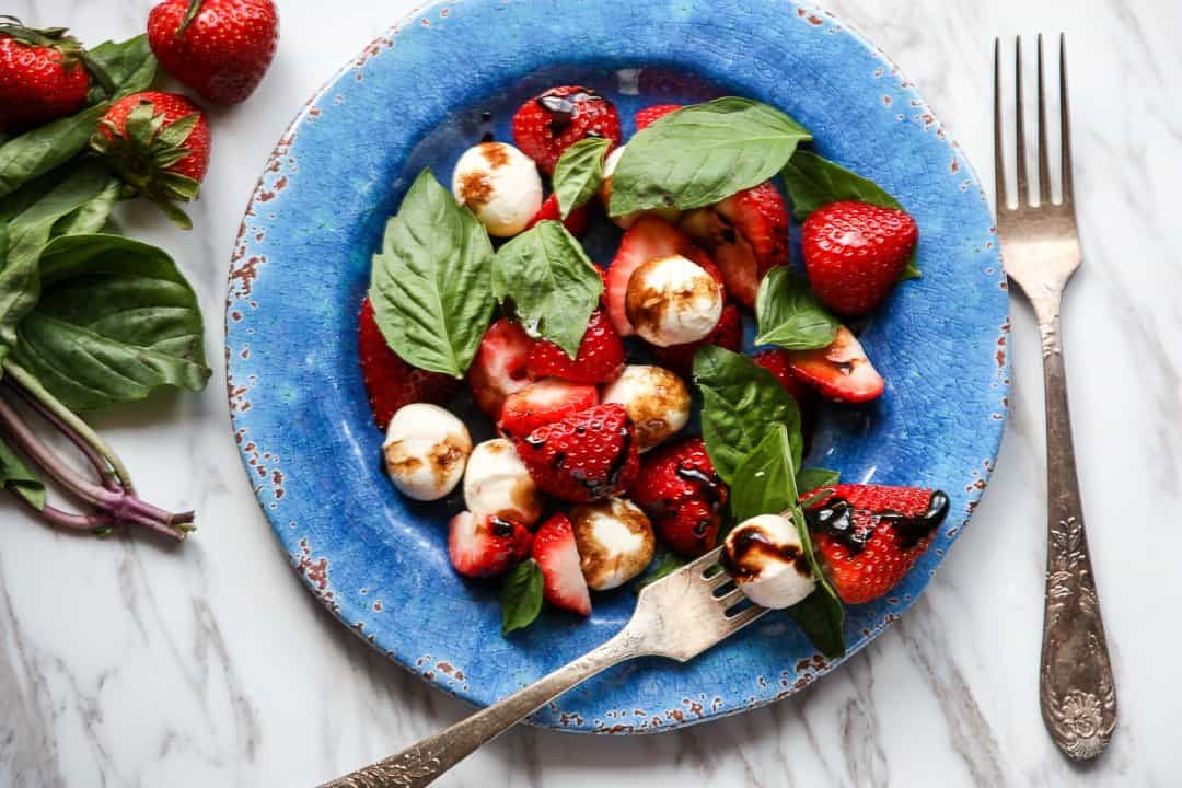 Strawberry caprese salad with fork on blue plate.