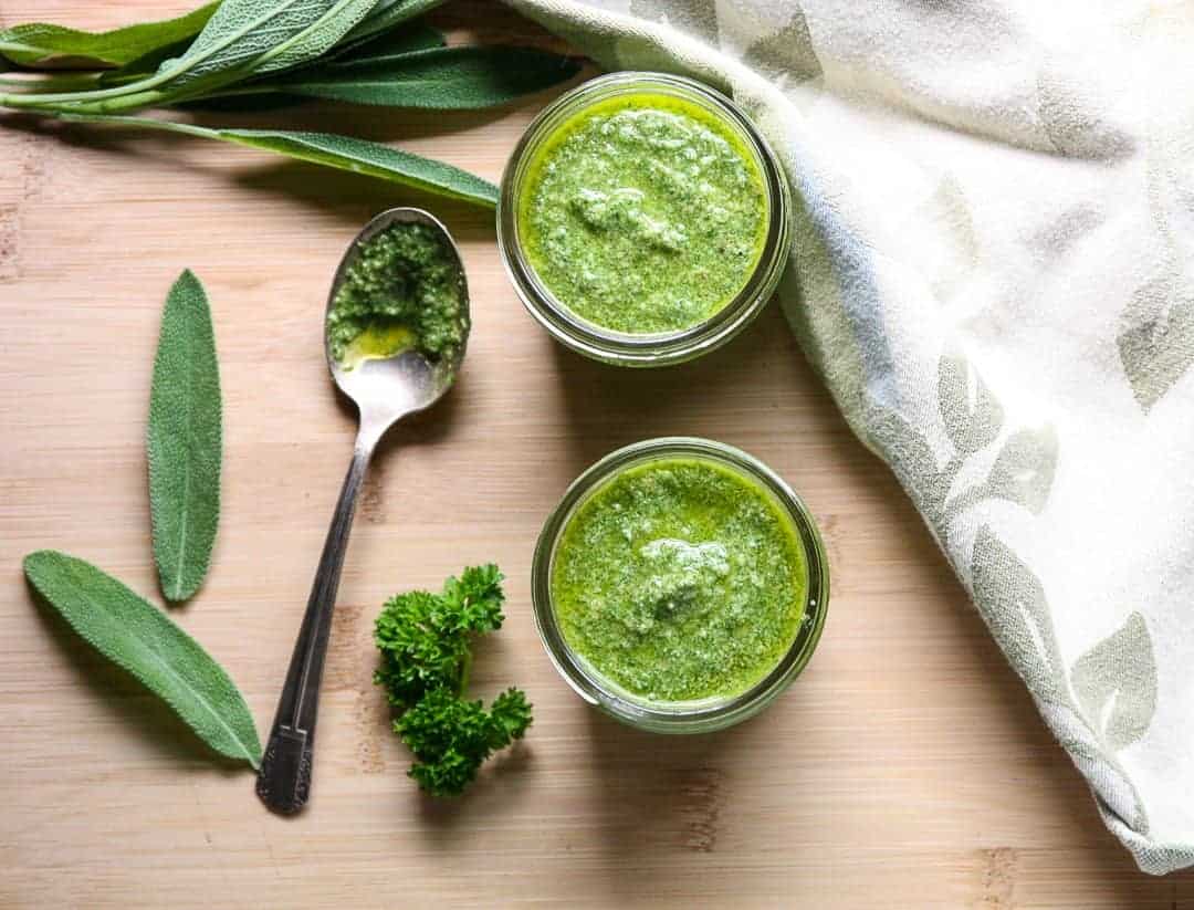 Two jars of pesto on a wooden cutting board