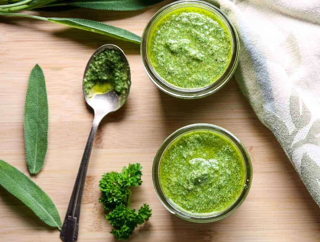 Two half pint jars of walnut sage pesto with sage and parsley leaves