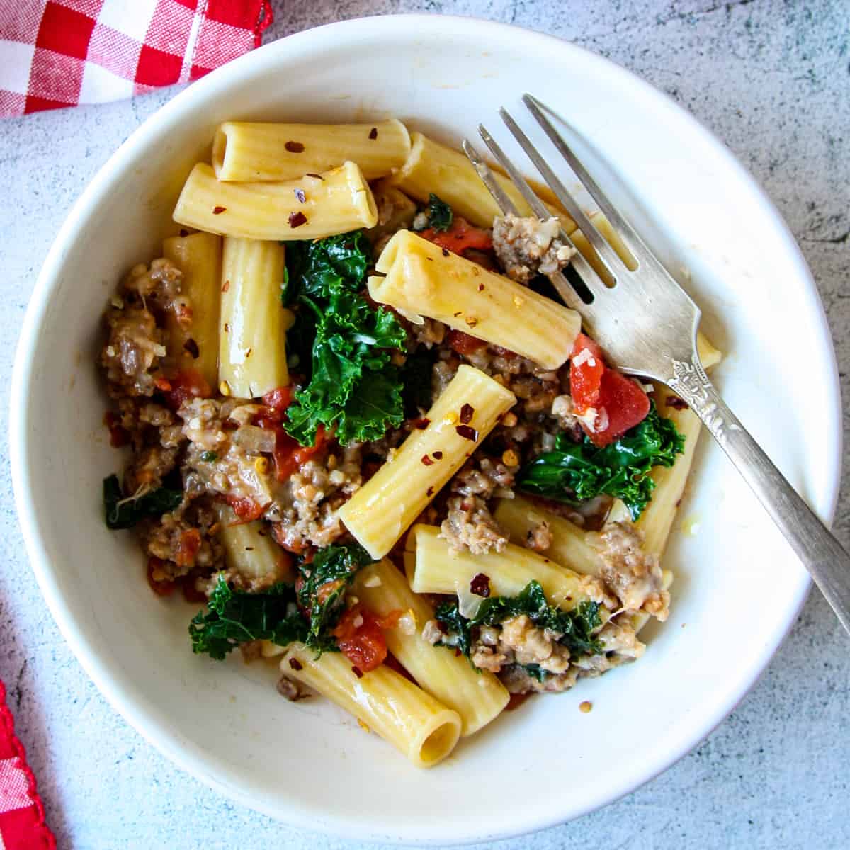 Sausage and kale pasta in a white bowl with a silver fork.