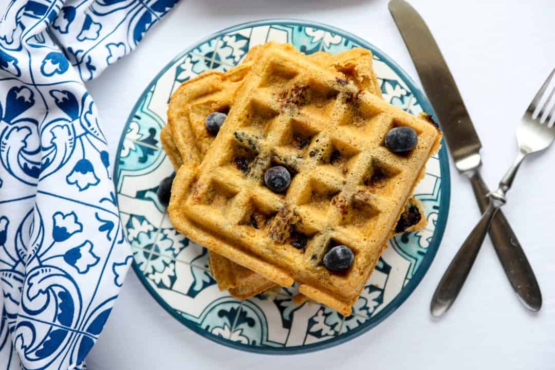 Blueberry coconut waffles on a blue and white patterned plate with a blue & white napkin, fork, and knife