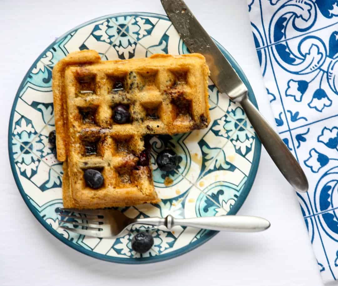A waffle on a plate with a slice cut out of it