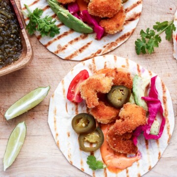 Coconut Shrimp Tacos with lime wedges on a cutting board.