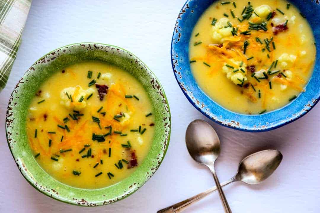 Two bowls of soup in blue and green bowls with two spoons