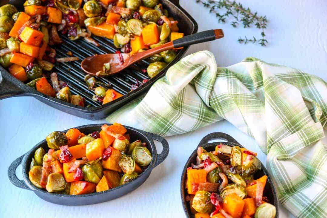 cast iron grill pan with roasted butternut squash, brussels sproups, cranberries & bacon, and two cast iron dishes of roasted vegetables