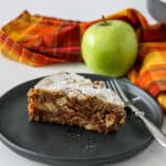 A slice of apple walnut cake on a black plate.
