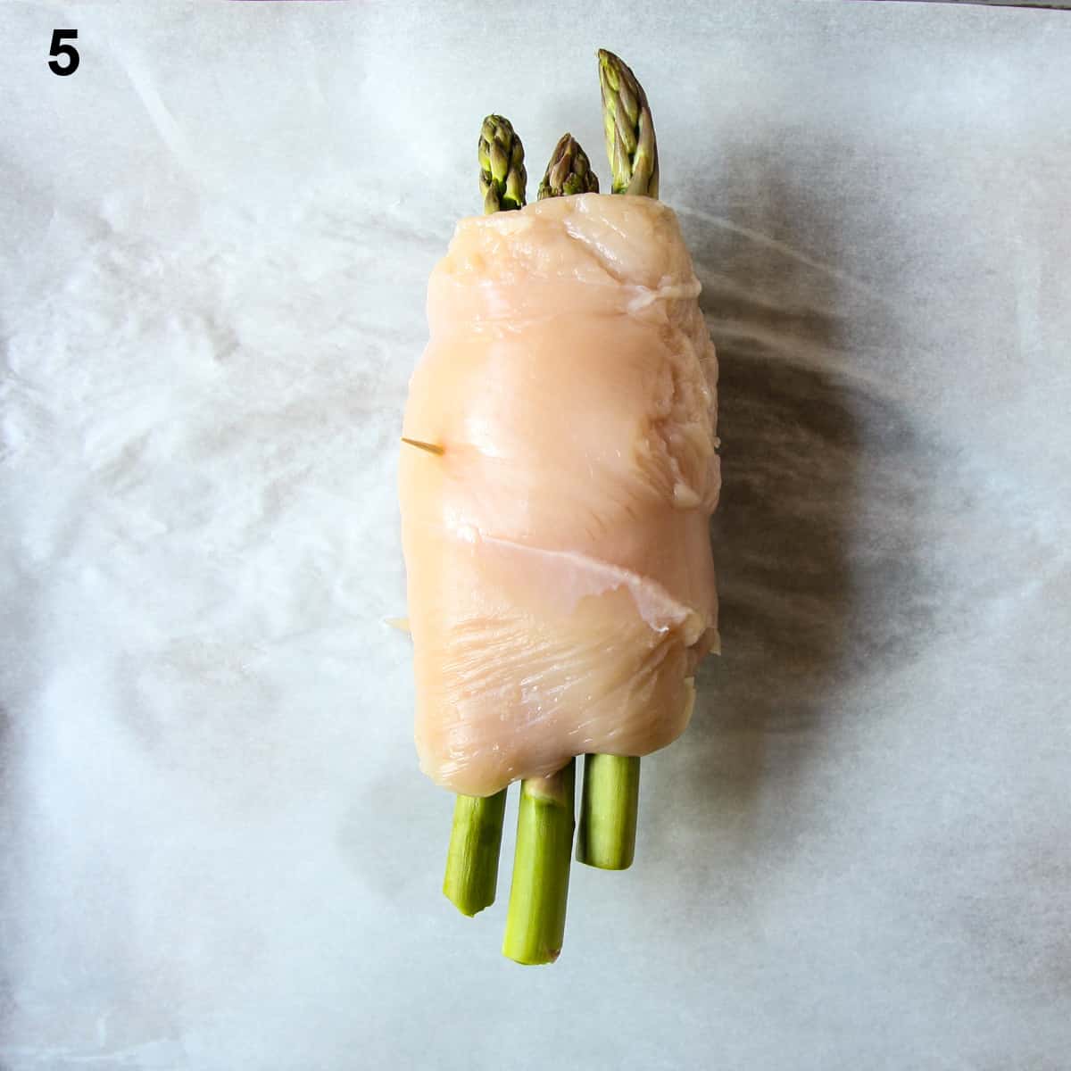Chicken breast being wrapped around asparagus and cheese.