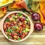 A bowl of fruit salsa on top of a wooden table, with Plums
