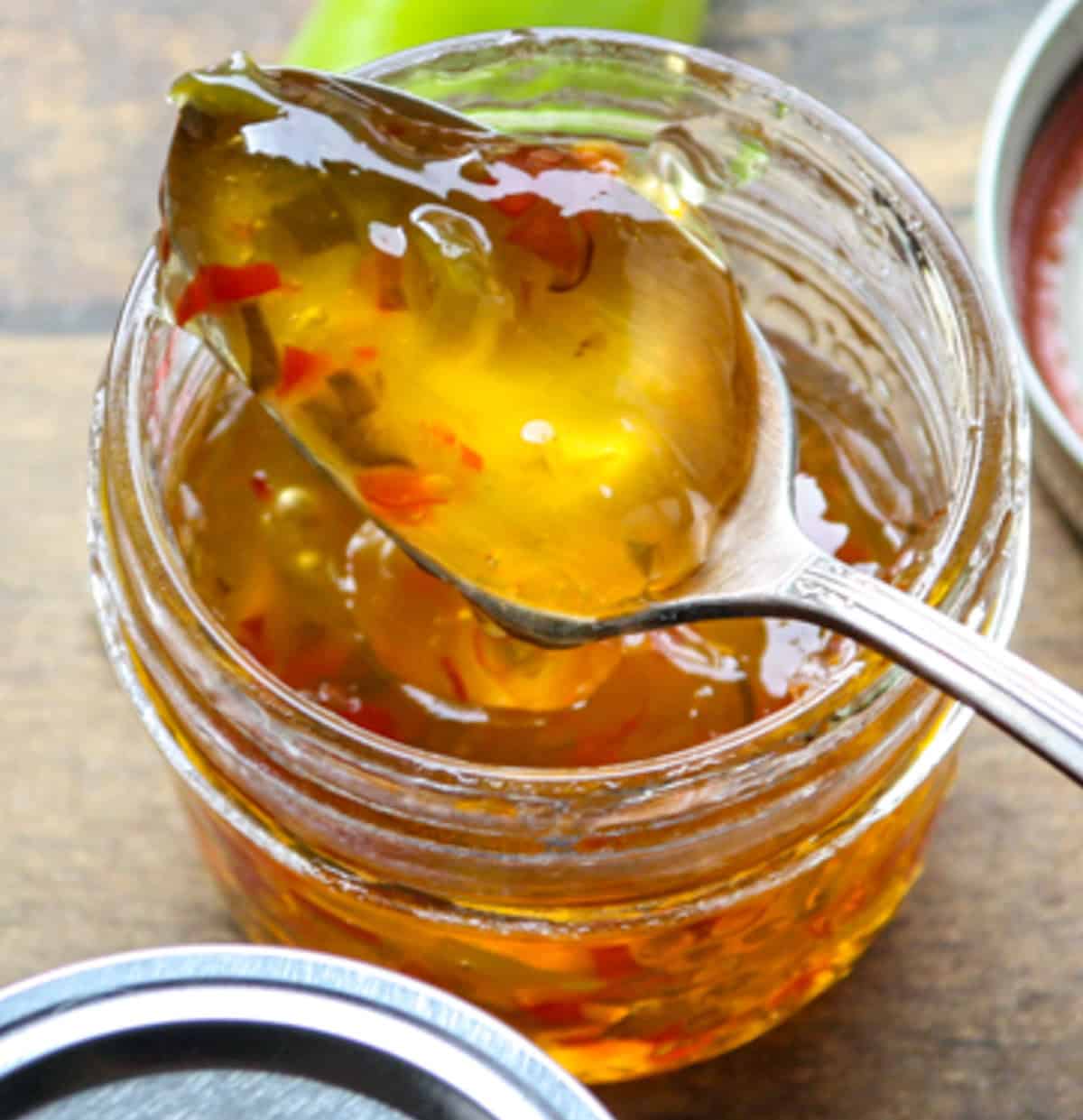 A glass jar of pepper jelly with a spoon inserted.