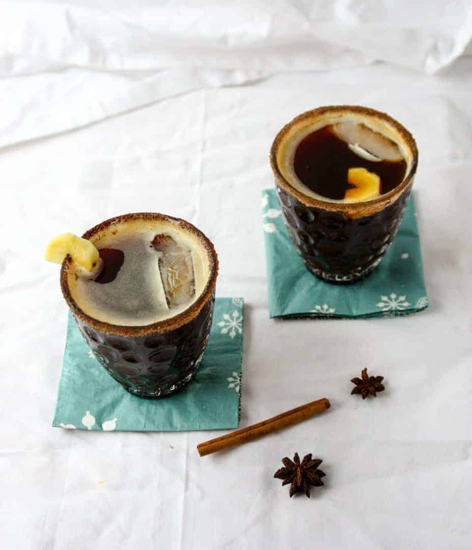 Two cocktails in glasses on blue napkins, sitting on top of a white table with cinnamon pieces nearby