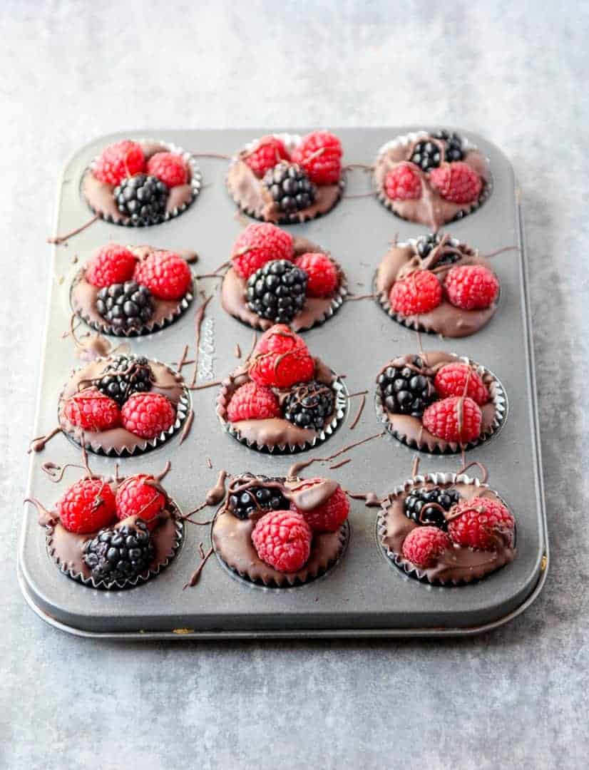 A twelve cup mini muffin tin filled with berry topped chocolates