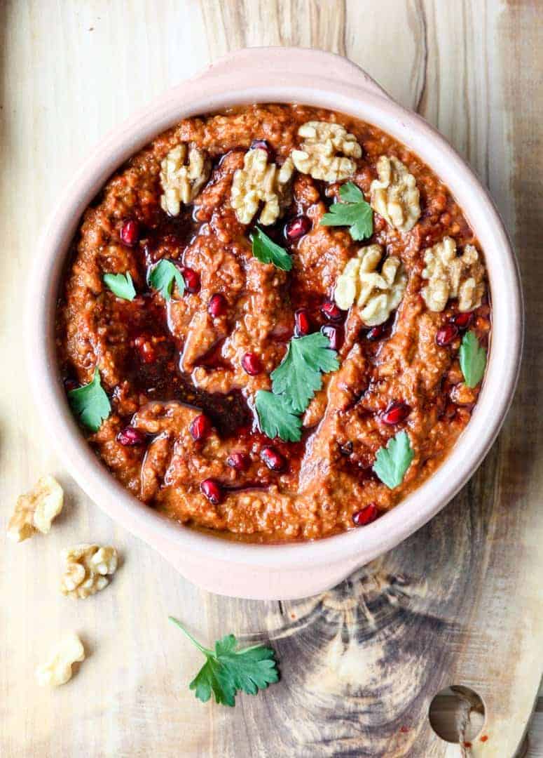 Muhammara di in a clay bowl drizzled with pomegranate molasses and garnished with walnuts