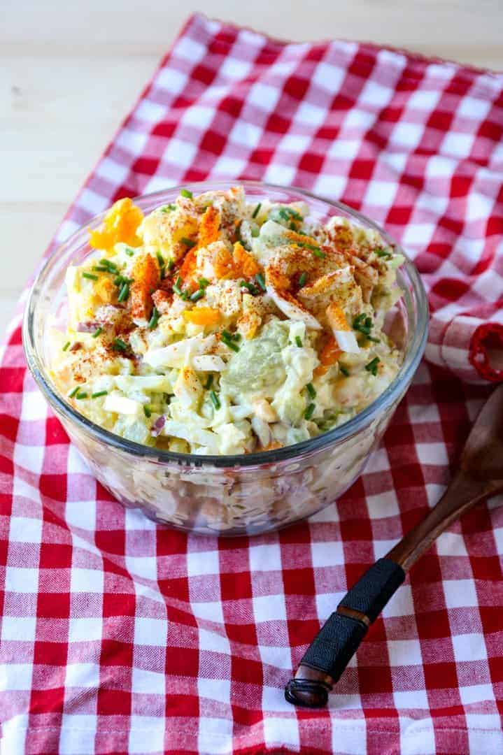 Glass bowl full of classic potato salad on a red & white checkered napkin