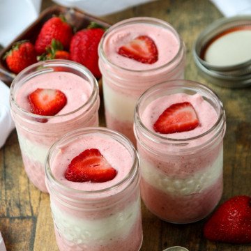 jars of mousse with pink and white layers topped with fresh strawberry slices in mason jars