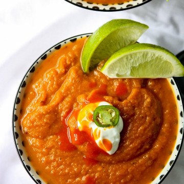A close up of a bowl of soup with lime wedges