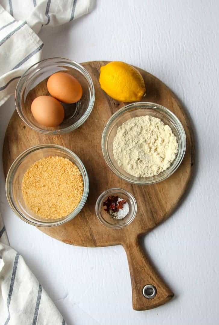 Bowls of bread crumbs, eggs, spices and a lemon on a wooden board