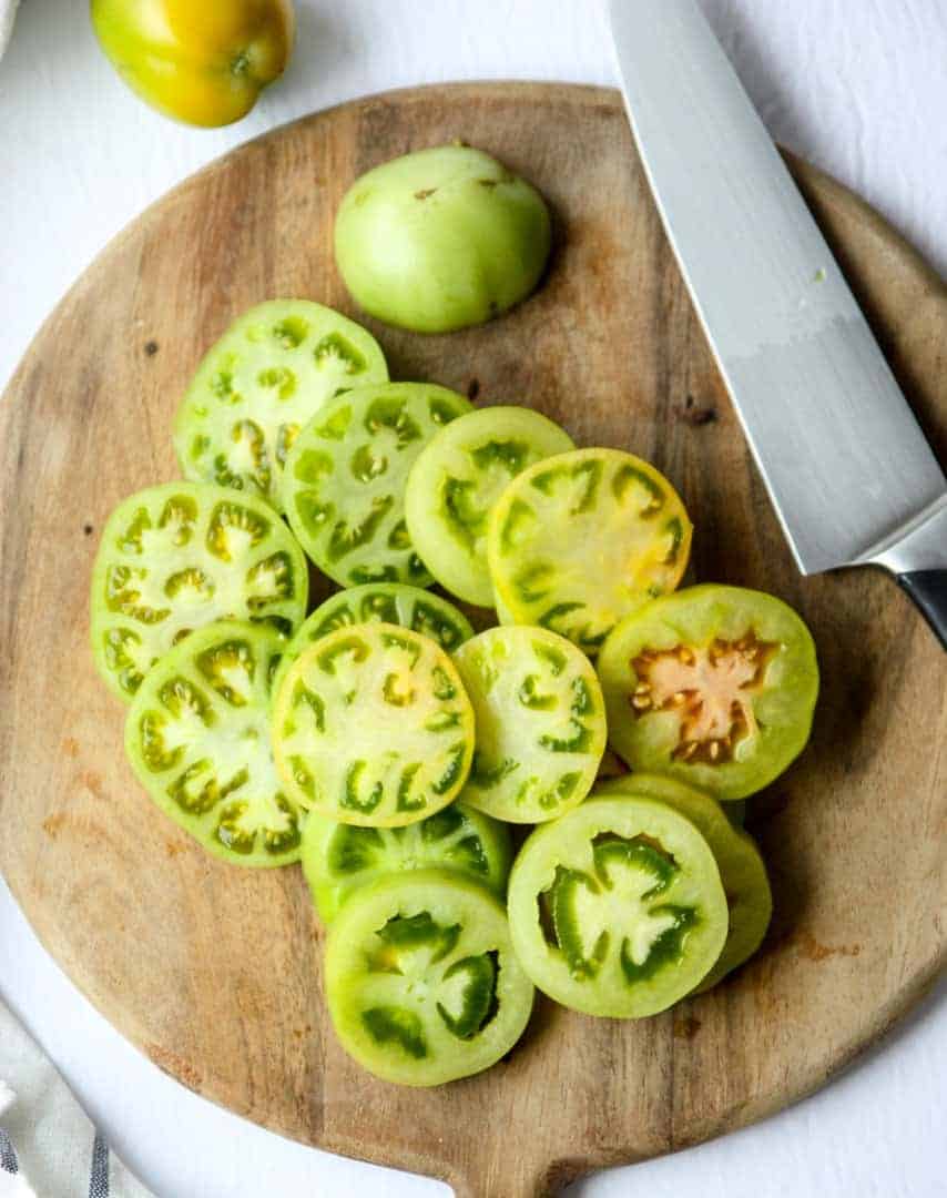 Green tomato slices on a cutting board with a knife