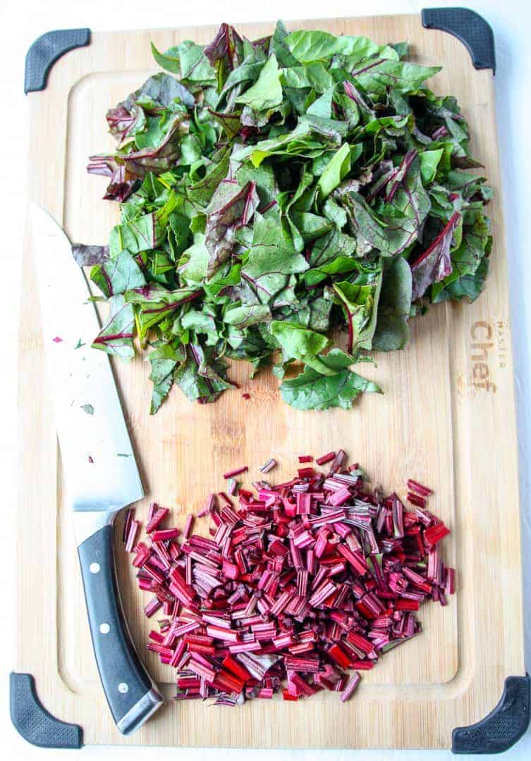 Chopped beet tops on a wooden cutting board with a knife.