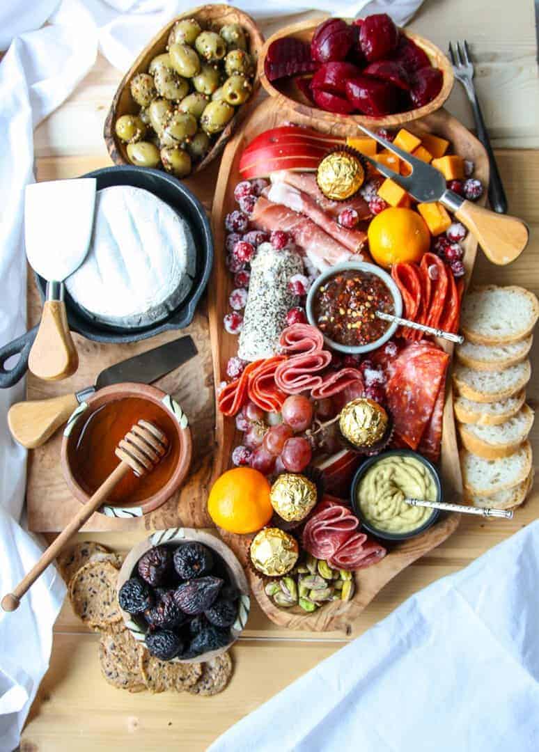 A wooden Holiday Charcuterie Board with various meats, cheeses, olives, nuts, chocolates and fruit.