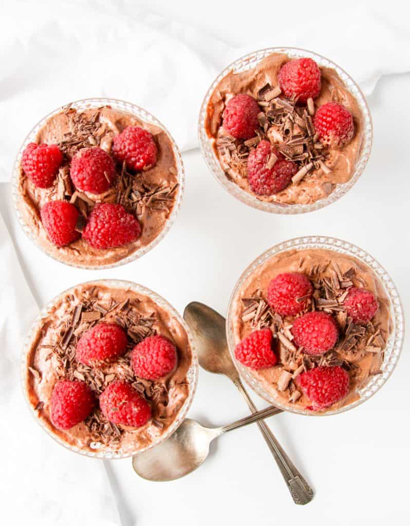 Four dessert dishes of chocolate mousse topped with raspberries.