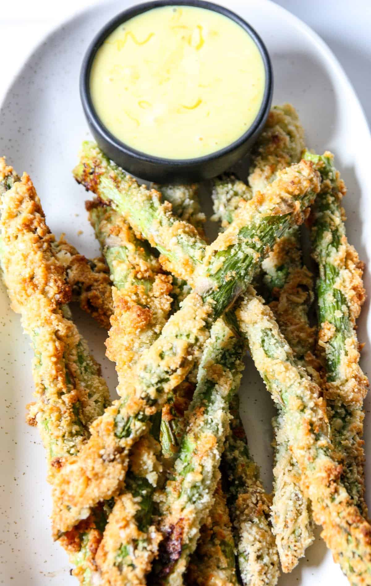 Air fried asparagus fries on a plate with a small dish of dipping sauce.
