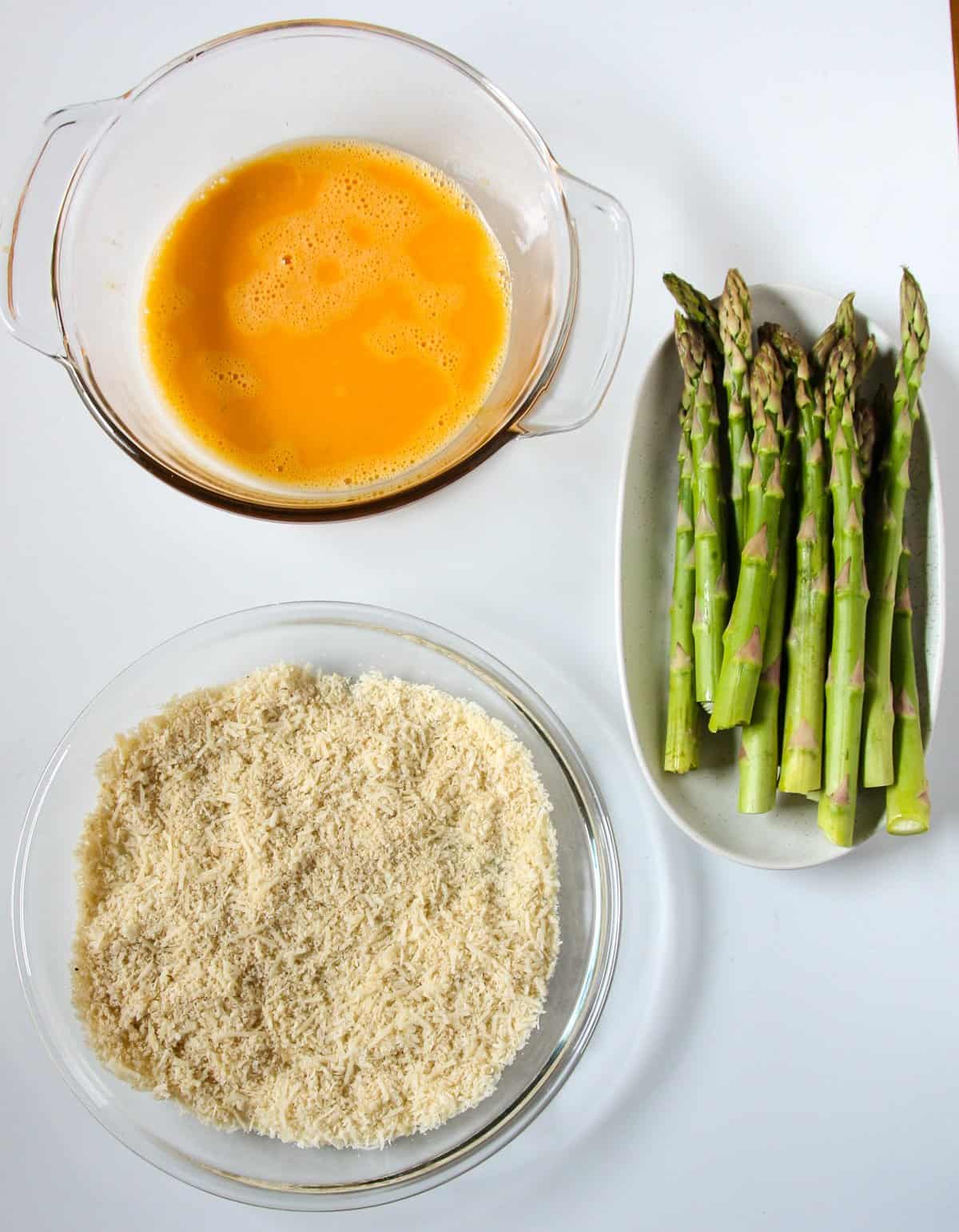 Dishes of ingredients ready for breading asparagus.