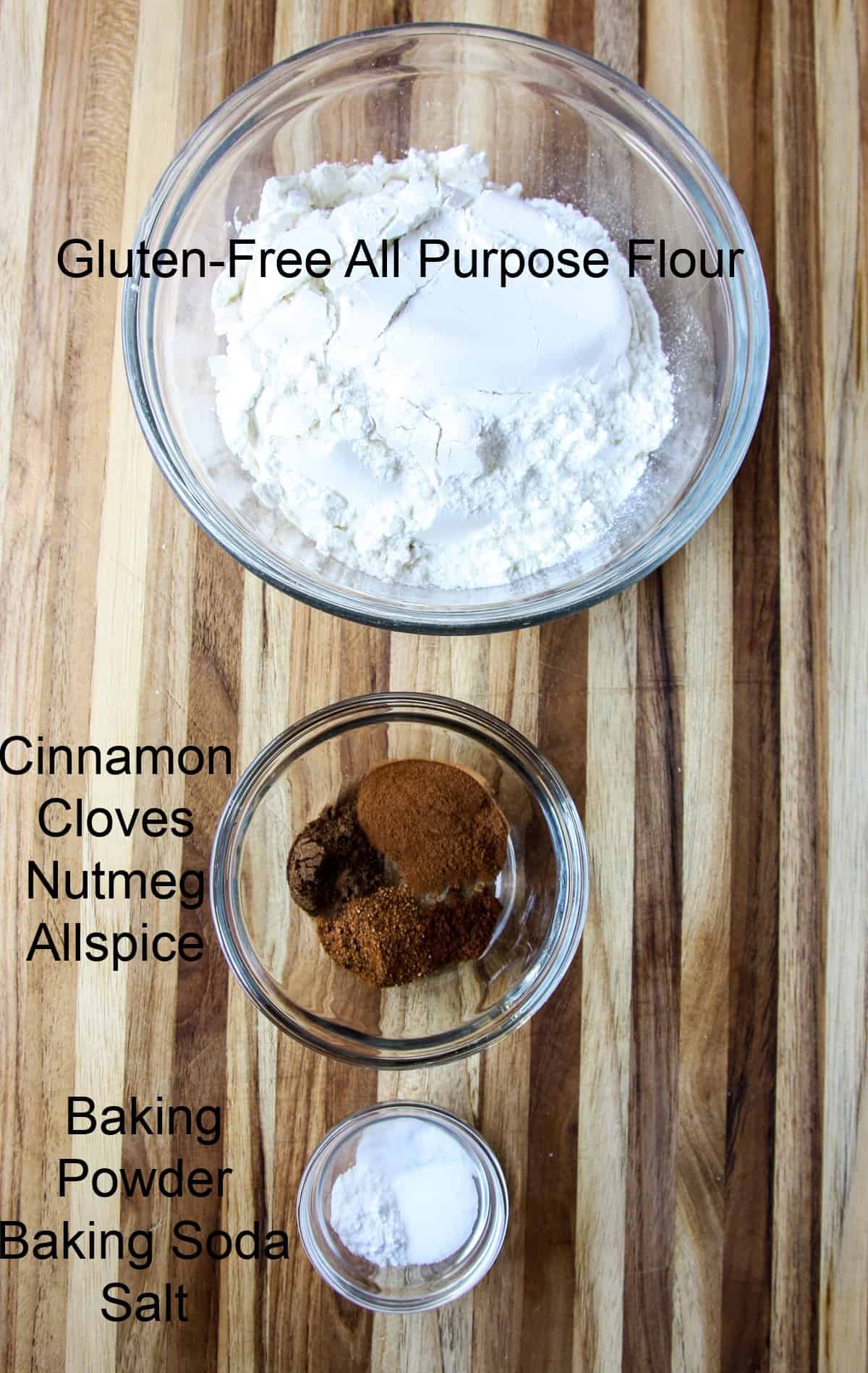 Three glass bowls filled with dry ingredients for the recipe, on a wooden cutting board.