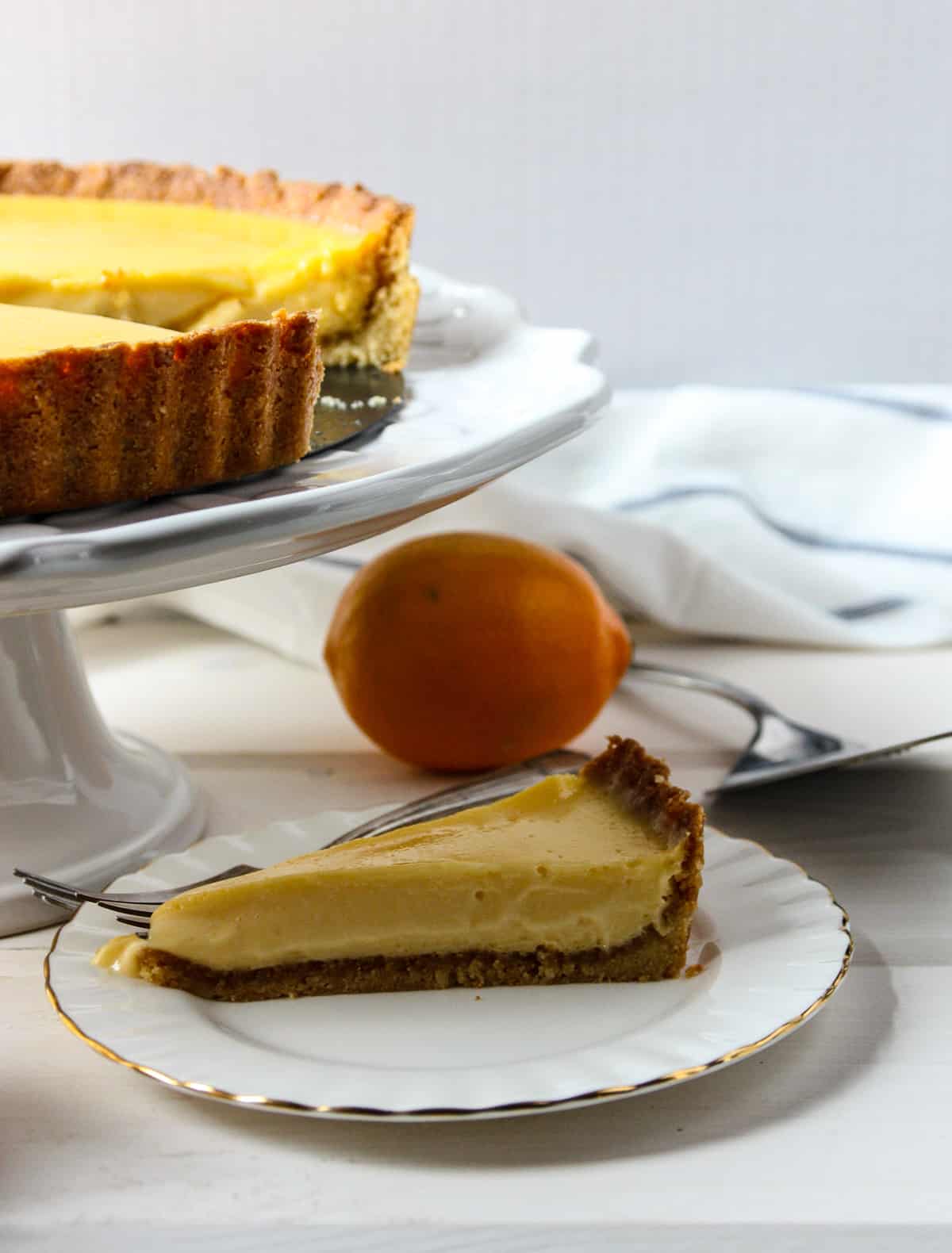 A lemon tart on a cake stand with a slice removed.