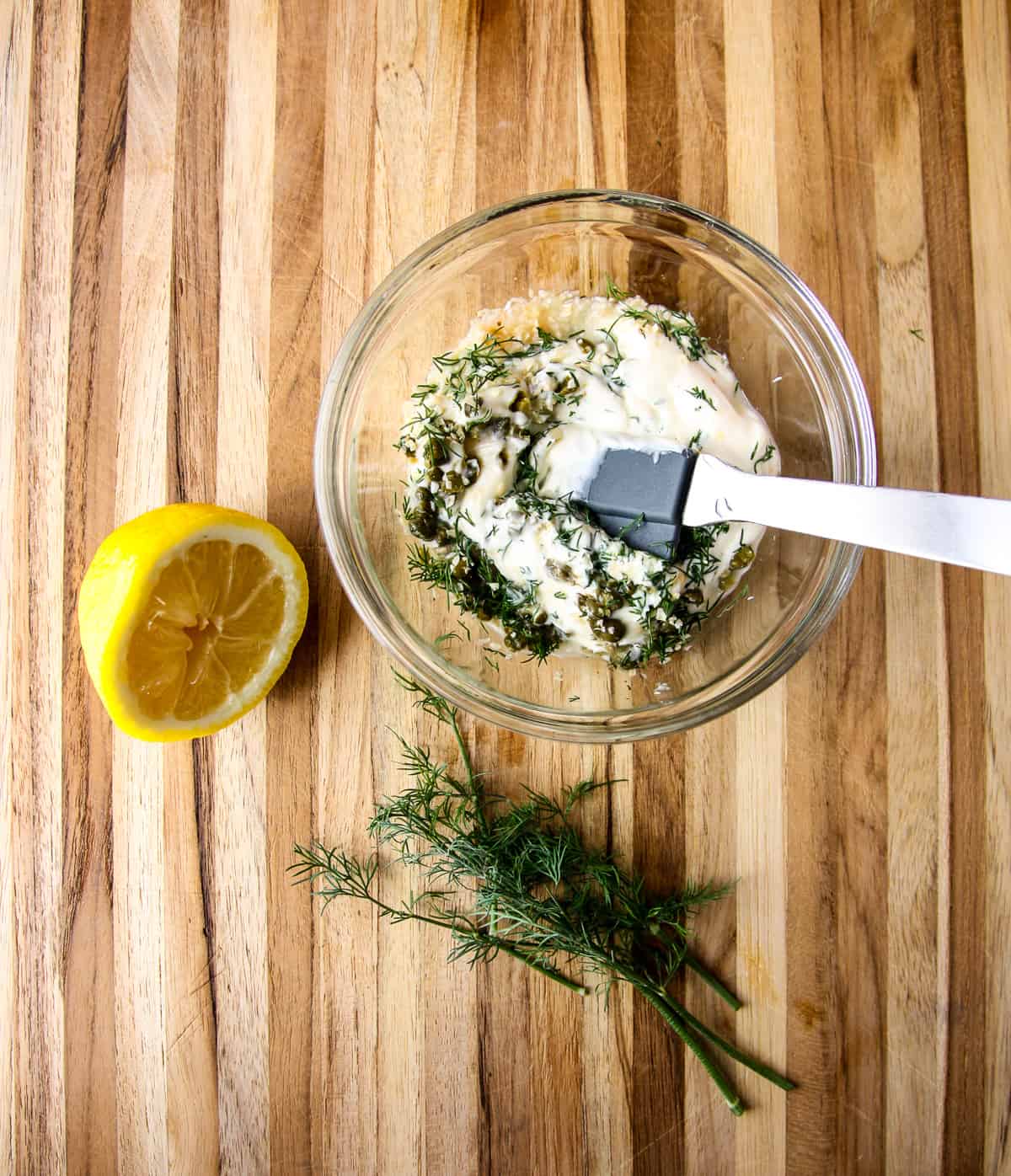 Ingredients for tartar sauce being stirred together in a glass bowl.