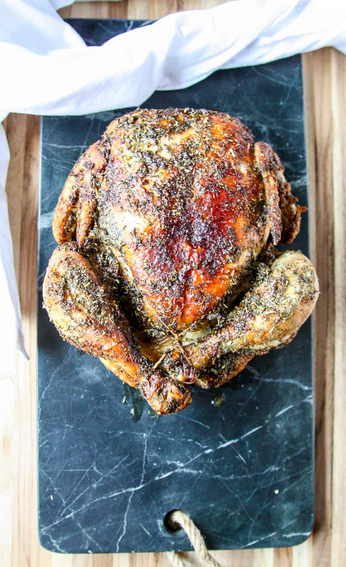 The cooked whole chicken resting on a marble board before being carved.