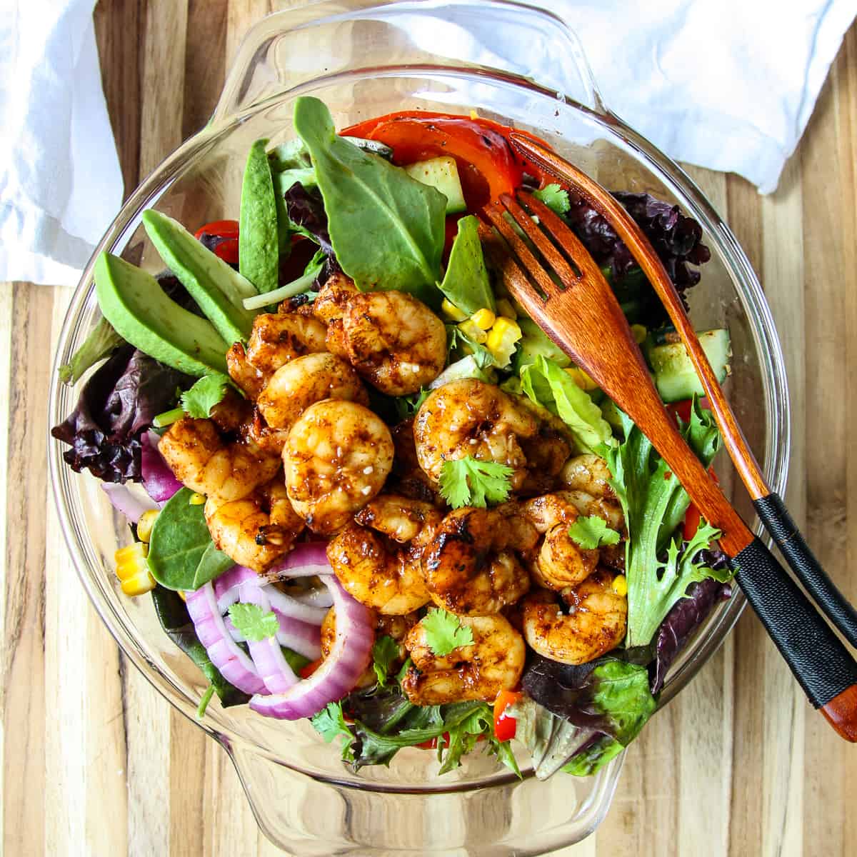 Grilled shrimp salad in a glass bowl with two wooden forks.