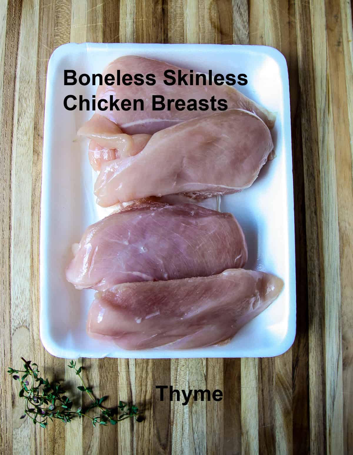 Raw chicken breasts and sprigs of thyme on a wooden board.