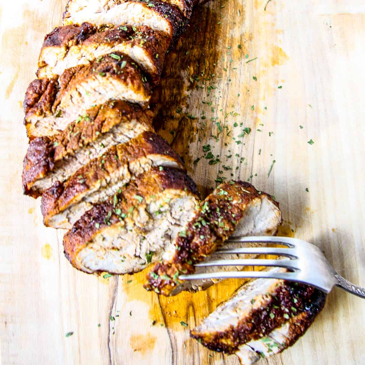Sliced pork tenderloin on a wooden cutting board.