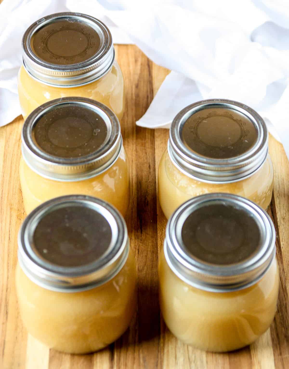 Five processed jars of applesauce on a wooden board.