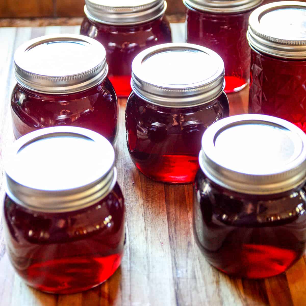 Seven jars of jelly on a wooden countertop.