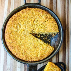 Cornbread in a cast iron skillet with one slice removed.