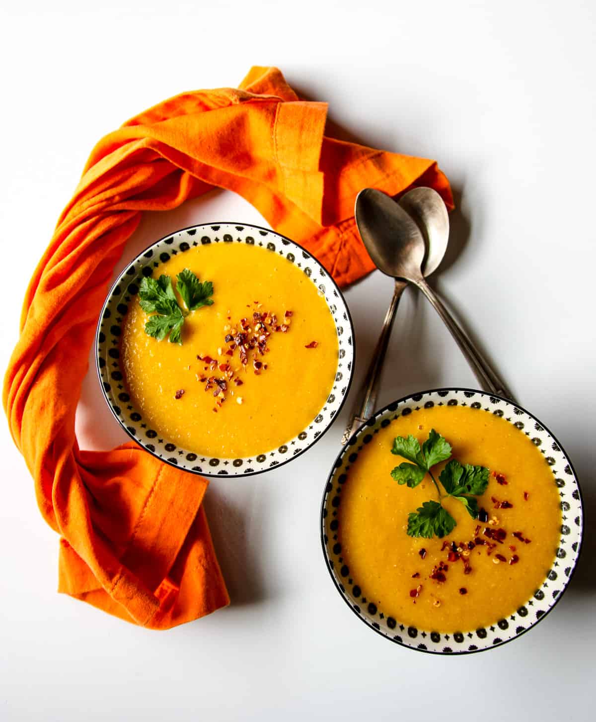 Two bowls of carrot and lentil soup and two spoons.