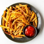Rutabaga fries on a black plate with a small dish of ketchup.