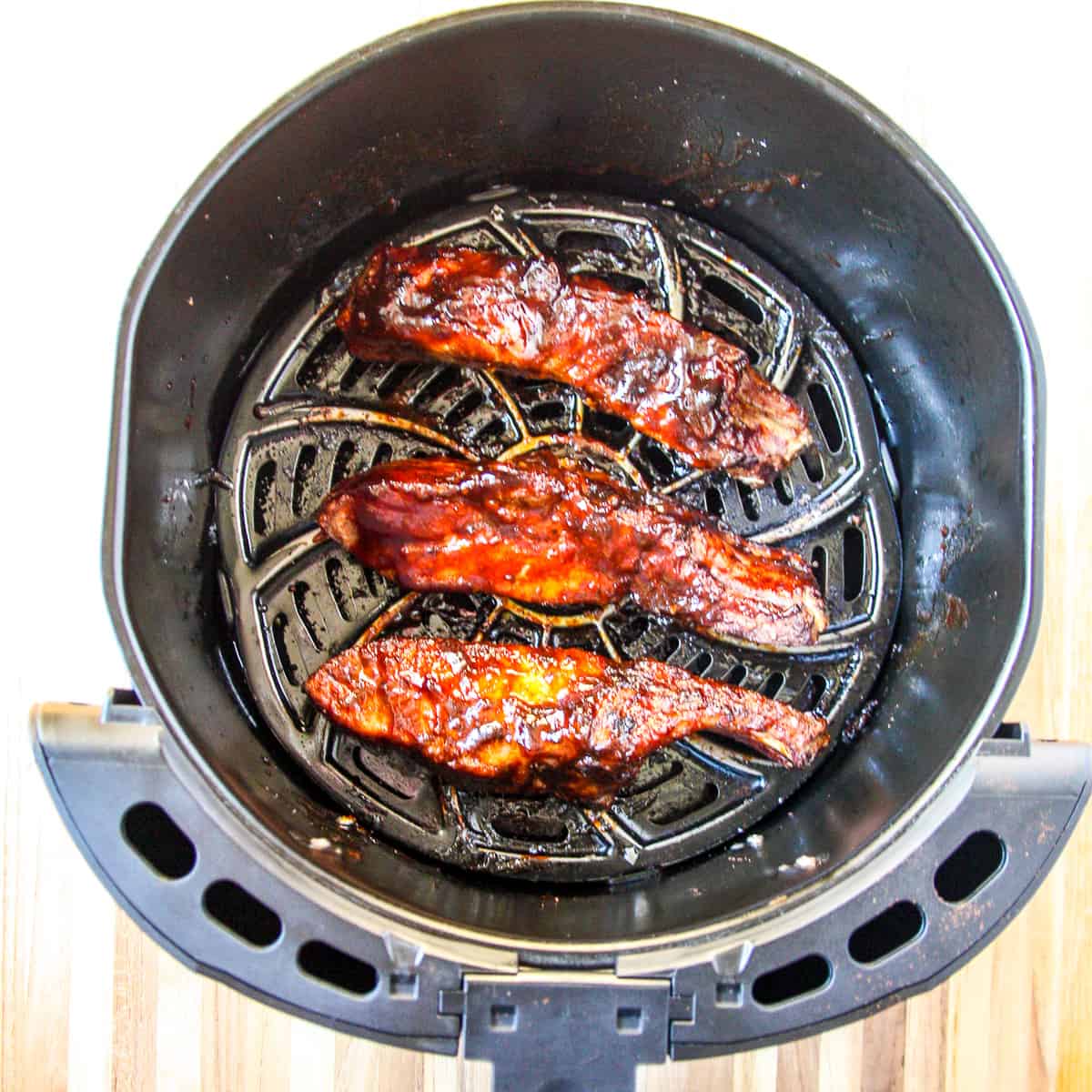 Cooked ribs brushed with barbecue sauce in an air fryer basket.