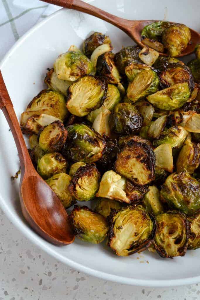 Crispy air fried brussels sprouts in a white bowl with a wooded spoon.