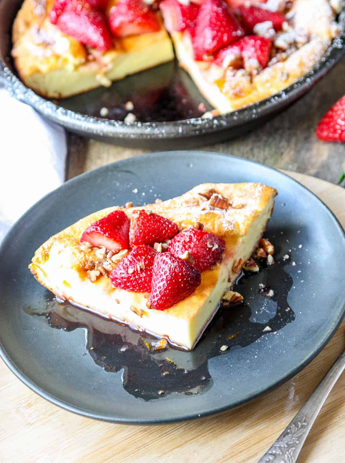 A slice of the pancake topped with strawberries on a black plate.