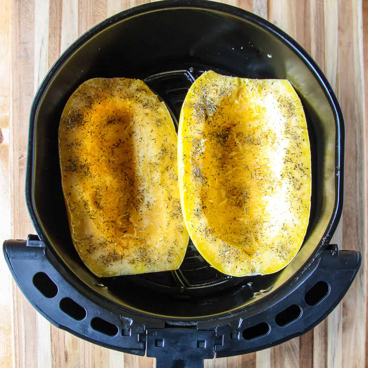 The two squash halves in the air fryer basket before cooking